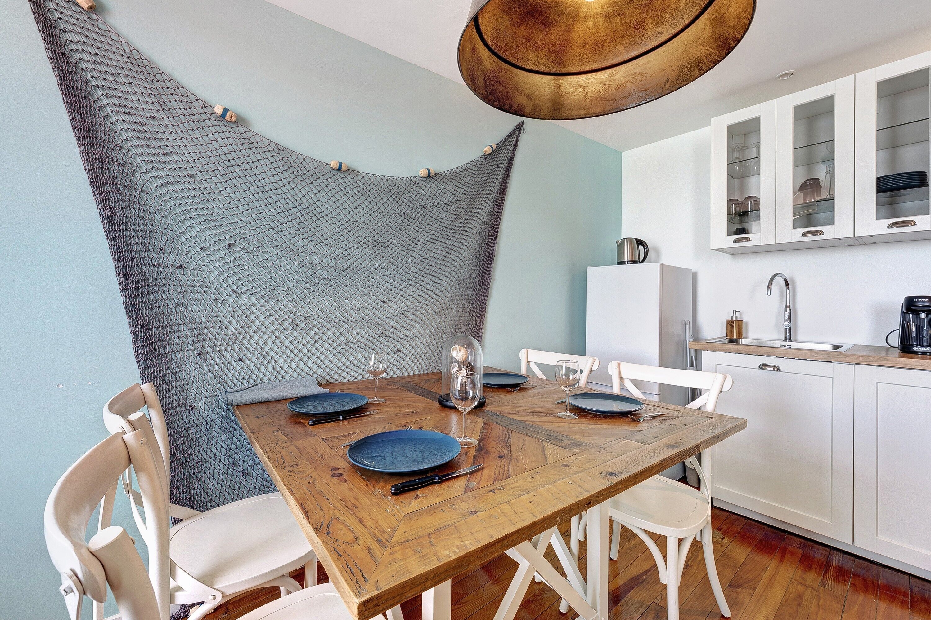 A dining area with a wooden table, white chairs, and a kitchen with white cabinets and a sink.