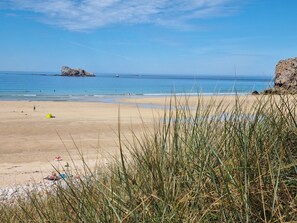 Une plage avec un ciel dégagé, une eau calme et des affleurements rocheux.