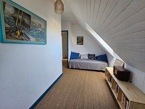 A bedroom with a sloped ceiling, a bed with blue and patterned pillows, a wooden bookshelf, and a framed painting on the wall. - House Overlooking Camaret with Harbor View (Camaret-sur-Mer)