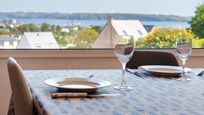Una mesa de comedor con platos, cubiertos y vasos, con vistas a un cuerpo de agua y edificios.