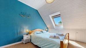 Un dormitorio con techo inclinado, cama con cabecera de madera, mesita de noche, lámpara y ventana.