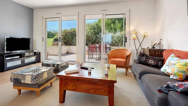 Una sala de estar con televisor, sofá, mesa de centro y vista a un patio exterior a través de puertas de vidrio.