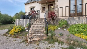 Een huis met een stenen trap, een balkon met metalen hekwerk en een tuin met diverse planten en bloemen.