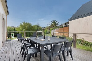 Um pátio externo com mesa retangular e cadeiras, ladeado por um deck de madeira.