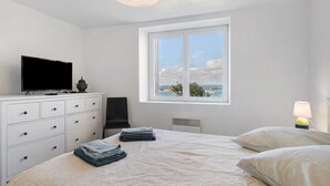 Une chambre à coucher comprenant un lit, un téléviseur, une commode, une chaise, une fenêtre donnant sur un beau paysage et une lampe.