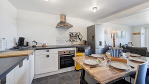 Une cuisine moderne avec des meubles blancs, une table à manger en bois et un four encastré.