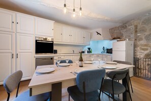 Een moderne keuken met witte kastjes, een eettafel voor vier personen en een stenen muur.