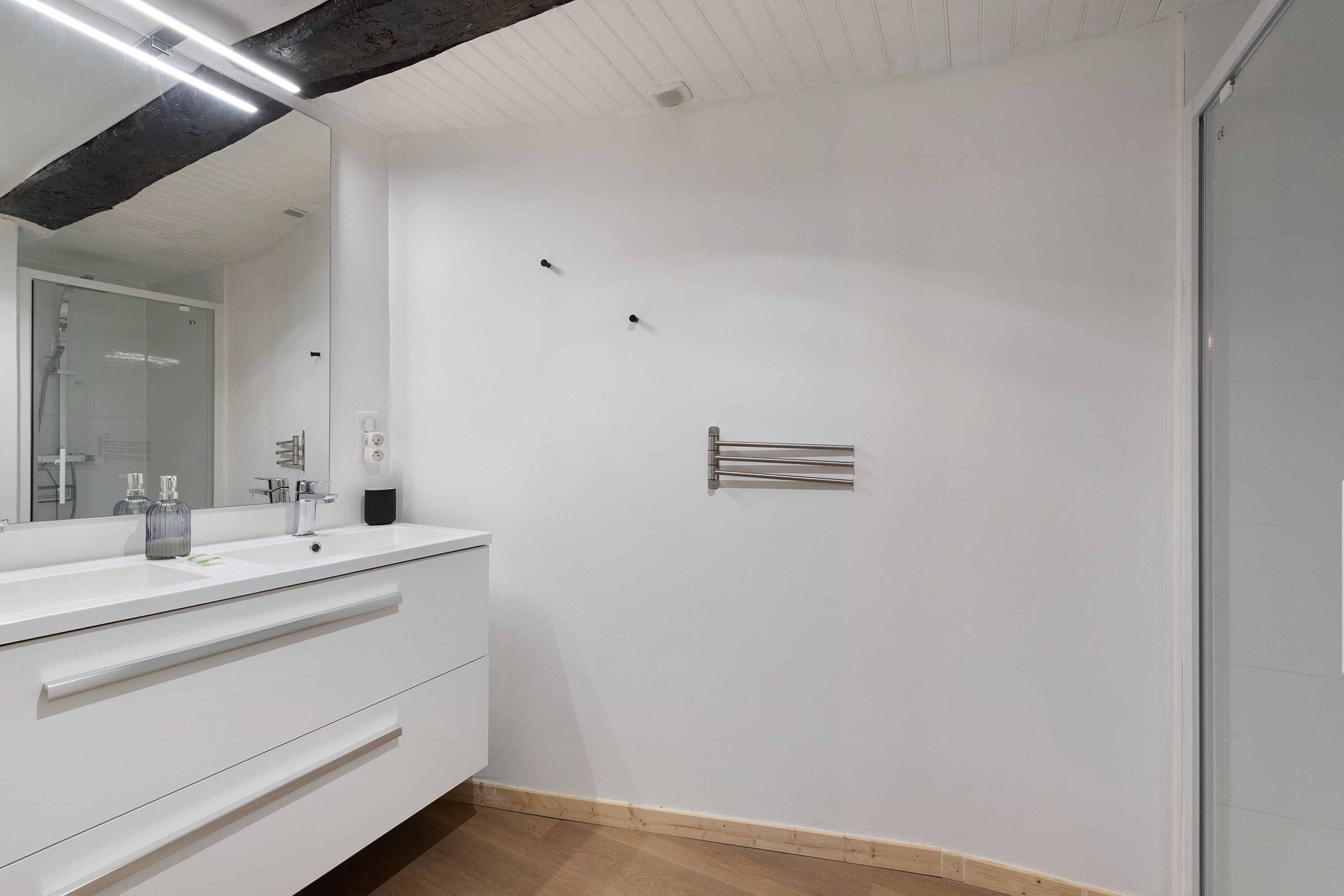 A modern bathroom with a white vanity, a large mirror, and a towel rack.
