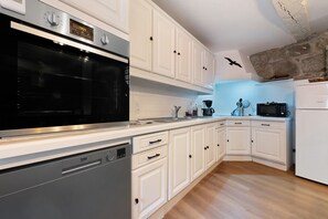 Une cuisine avec des meubles blancs, un four noir, un lave-vaisselle, un four à micro-ondes et un réfrigérateur.