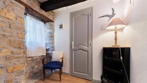 Quarto com parede de pedra, uma cadeira de madeira, uma porta cinzenta e uma estante preta.
