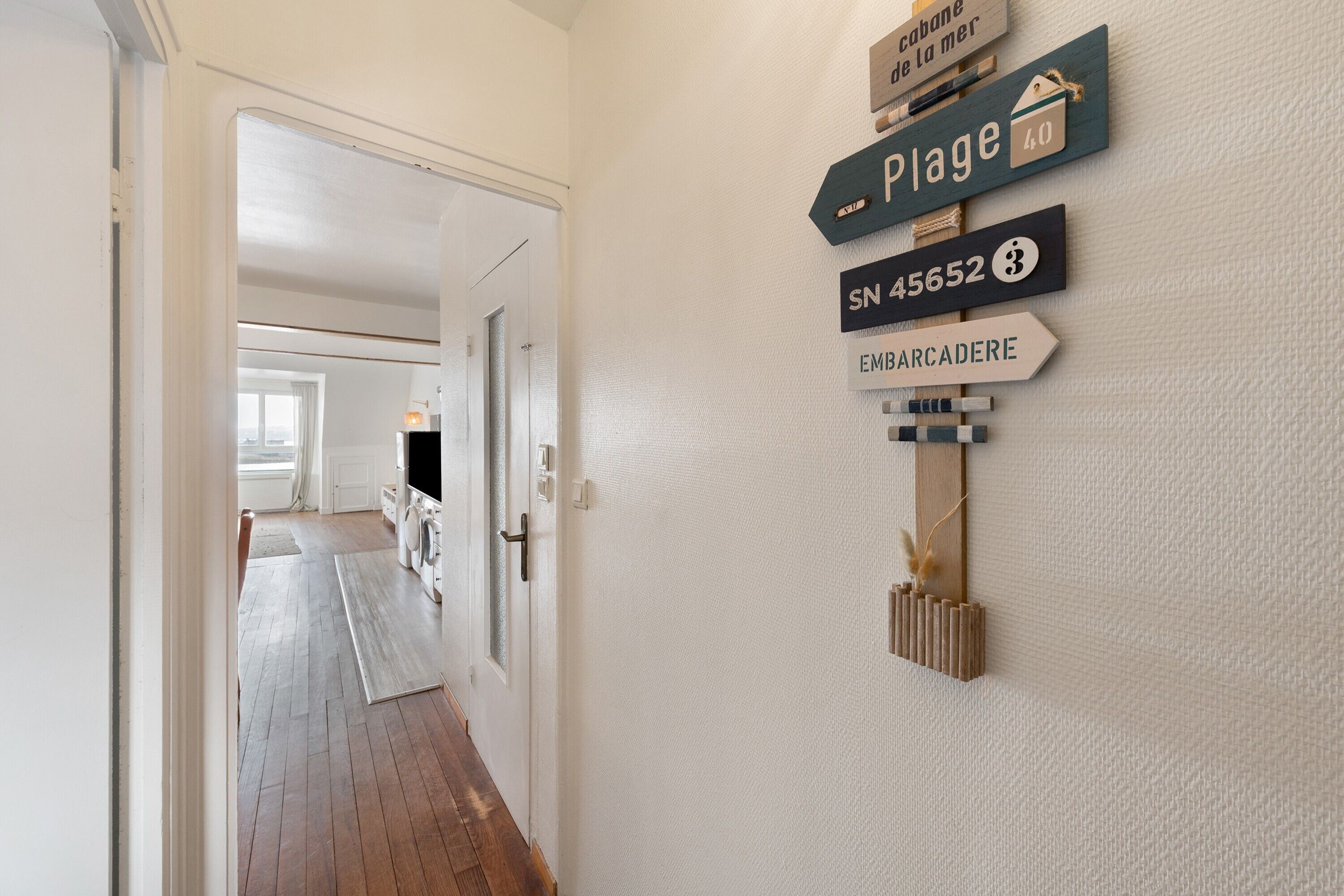 A hallway with wooden flooring, a door leading to a room, and a wall-mounted signpost with directional signs.