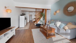 Un salon moderne doté d’un téléviseur à écran plat, d’une table basse en bois, d’un canapé gris et d’un escalier menant à la cuisine.