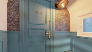 Une porte bleue avec une poignée en laiton et une plaque nominative, un escalier et un mur orné d’un motif représentant une carte.
