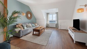 Un salon de style industriel, avec un canapé, une table basse et un meuble pour la télévision, un plancher en bois et une grande fenêtre agrémentée de rideaux.