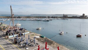 Un port de plaisance avec des bateaux, une grue et des espaces de détente en plein air, ombragés par des parasols.