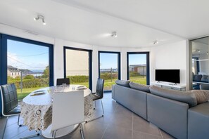 Una sala de estar moderna con comedor, ventanas grandes y un televisor de pantalla plana.