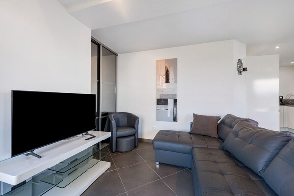 Una sala de estar moderna con un televisor de pantalla plana, un sofá gris, un sillón gris y una mesa de centro de vidrio.