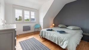 Un dormitorio con cama, ventana, silla, escritorio y lámpara.
