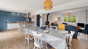 Una cocina moderna con gabinetes blancos, un comedor con una mesa dispuesta para seis personas y una sala de estar con sofá y televisor.