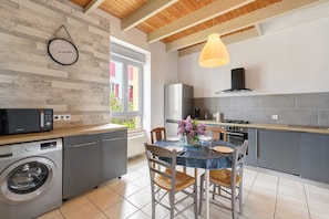 A modern kitchen with a built-in washing machine, a dining area with a table and chairs, and a large window. - Sea View, Authentic Fisherman's House (Camaret-sur-Mer)