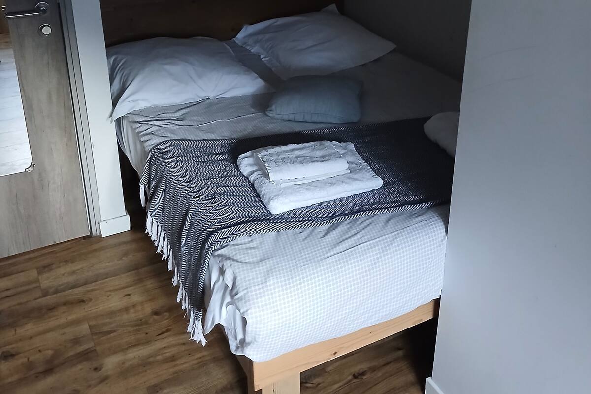 A small, compact bedroom with a wooden bed frame, a single bed, and a white air conditioning unit mounted on the wall.