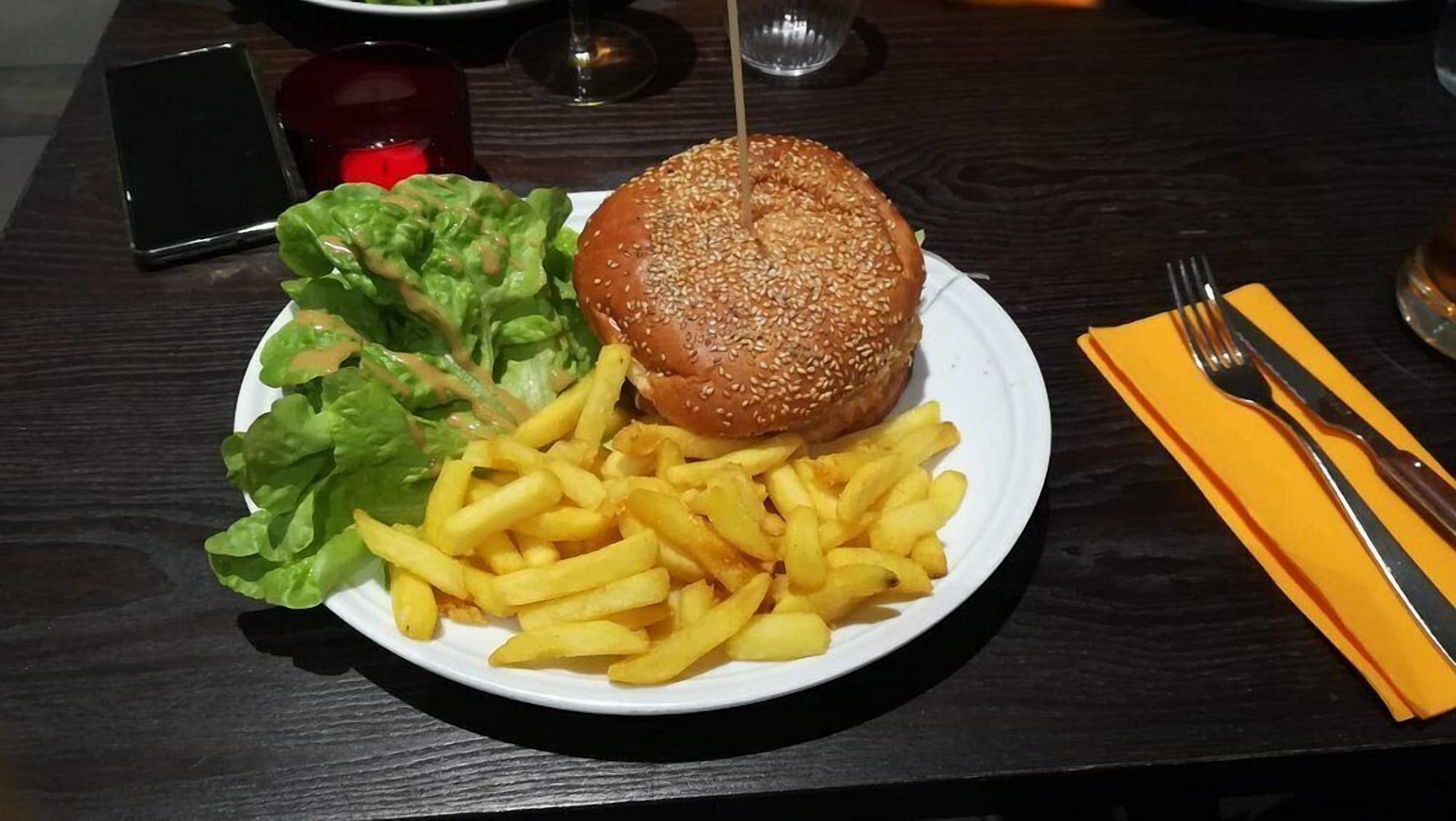 Une assiette contenant un hamburger, des frites et une salade, posée sur une table en bois.