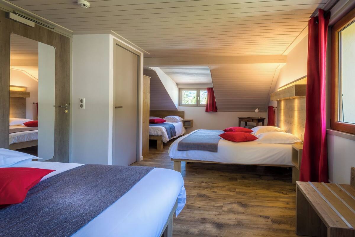 A room with three beds, wooden flooring, and a sloped ceiling.
