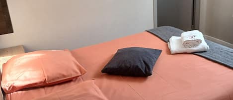 Un lit simple avec une couette orange, un oreiller foncé et une serviette blanche pliée.