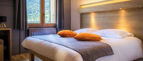 A neatly made bed with white and orange pillows, a wooden headboard, and a window with curtains.
