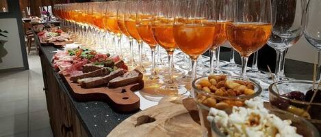Una larga mesa con múltiples vasos de líquido ámbar, diferentes tipos de comida y una tabla de madera.