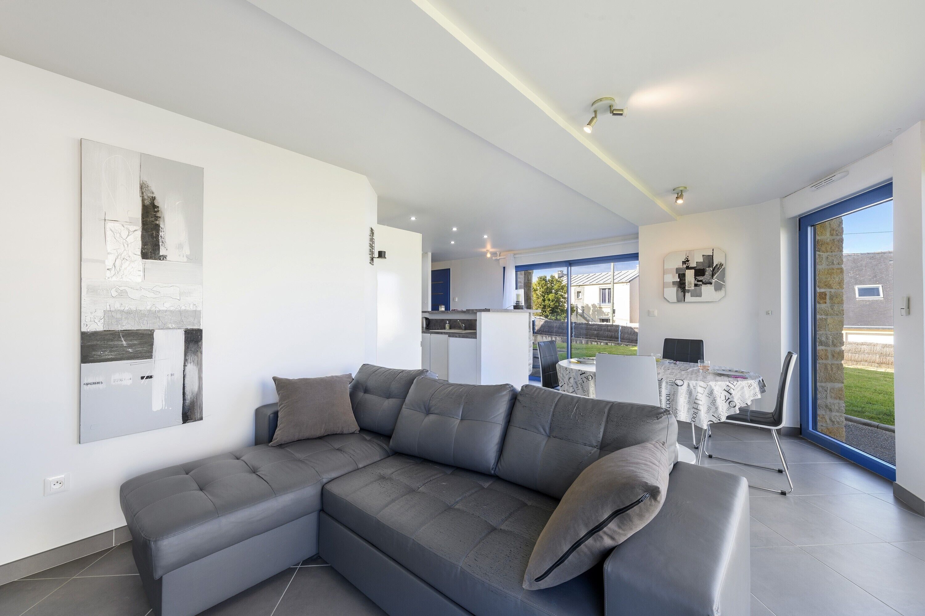 Ein modernes Wohnzimmer mit einer Eckcouch, einem Essbereich mit Tisch und Stühlen und Blick durch eine Glastür.