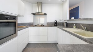 A modern kitchen with white cabinets, a stainless steel range hood, a double sink, and a built-in oven. - Magical Moments by the Sea (Camaret-sur-Mer)