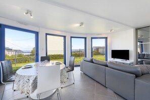 Ett modernt vardagsrum med en stor TV, en grå soffa och en matplats med ett bord och stolar.