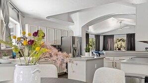 A modern kitchen with white cabinets, a central island, and a dining area with a vase of flowers.