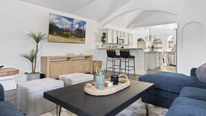 A modern living room with a sofa, ottoman, and coffee table, a wooden cabinet, and a painting of a mountain landscape.
