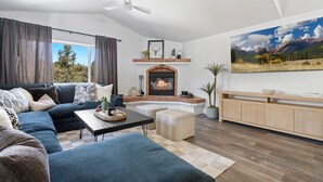 A modern living room with a fireplace, a large sofa, a coffee table, and a painting of a mountain landscape.