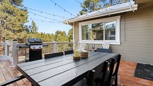 An outdoor deck with a grill, a table with chairs, and a window overlooking a wooded area.