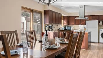 A dining area with a wooden table and chairs, a chandelier, and a kitchen with wooden cabinets and appliances.