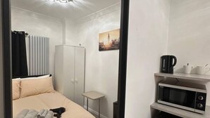 A compact hotel room with a bed, a small table, a microwave, and a picture of a cityscape on the wall. - London Borough 5 min walk (Greater London)