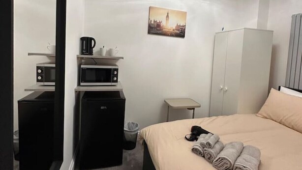 A hotel room with a bed, a mirror, a microwave, a small table, a cabinet, and a picture on the wall. - London Borough 5 min walk (Greater London)