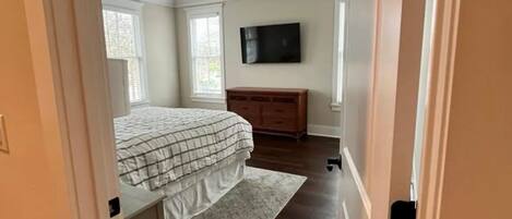 A bedroom with a bed, dresser, TV, and ceiling fan.