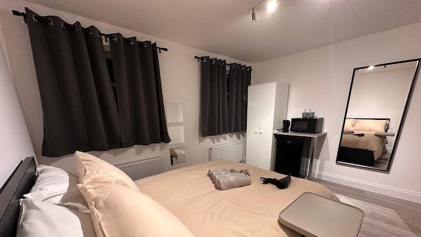 A hotel room with a bed, a bedside table, a mirror, a wardrobe, and a small kitchenette area. - Central London 5 min to metro (Greater London)