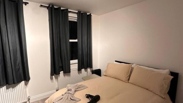 Een slaapkamer met een bed, een radiator, een raam met gordijnen en een plafondlamp.