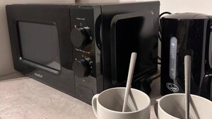 Een keukenhoek met een magnetron, een koffiezetapparaat en twee witte mokken met lepels.