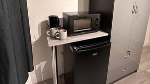 Una kitchenette compacta con microondas, un refrigerador pequeño y una cafetera sobre la encimera.