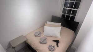 Ein Schlafzimmer mit Bett, Kissen, Nachttisch, Fenster und Tür.