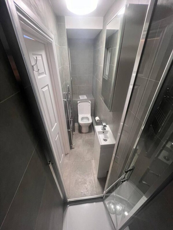 Ein schmales, modernes Badezimmer mit Toilette, Waschbecken und Dusche.