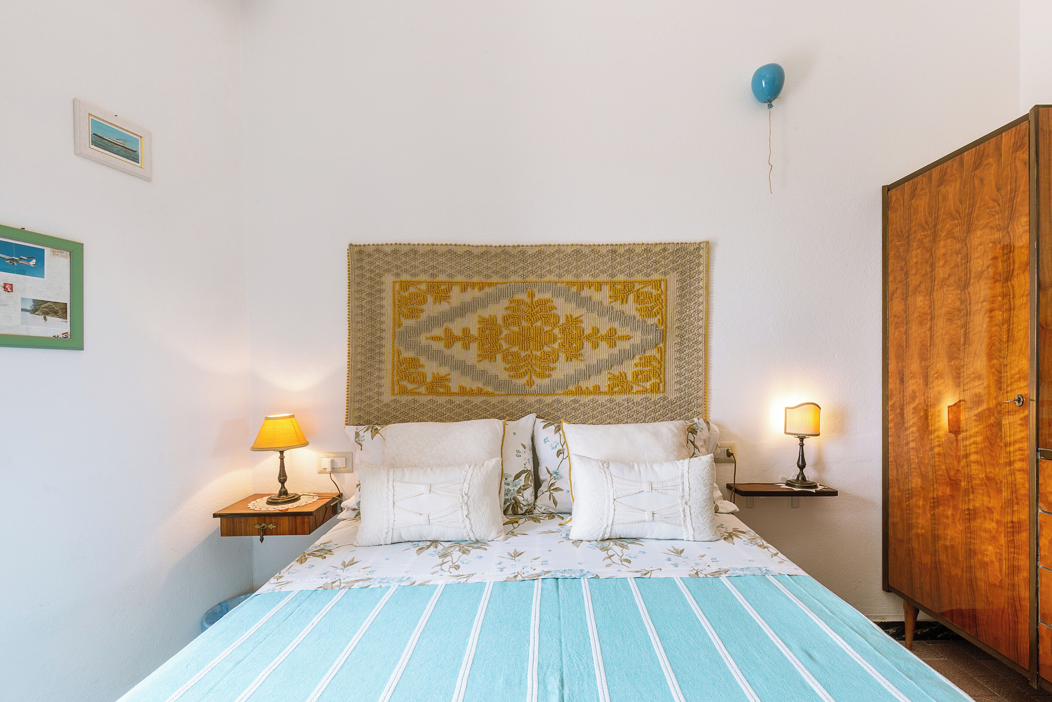 Une chambre à coucher avec un lit, deux tables de chevet avec des lampes, une armoire en bois et une tapisserie au mur.