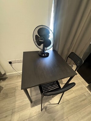 A small table with a black fan, a chair, and a power outlet on the wall. - Flat with Bathroom and Kitchen (Greater London)