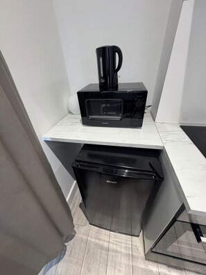 Eine kompakte Küchenzeile mit Mikrowelle, Kaffeemaschine und kleinem Kühlschrank.